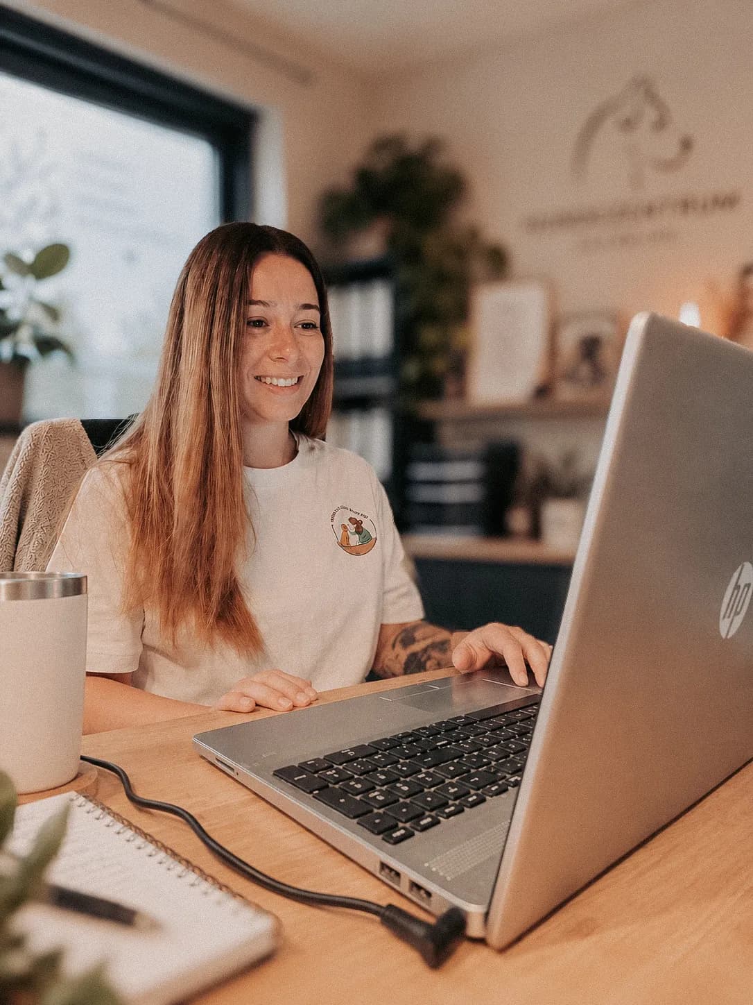 Lisah sitzt im Büro des Hundezentrums am Laptop und lächelt beim Online-Training in den Bildschirm